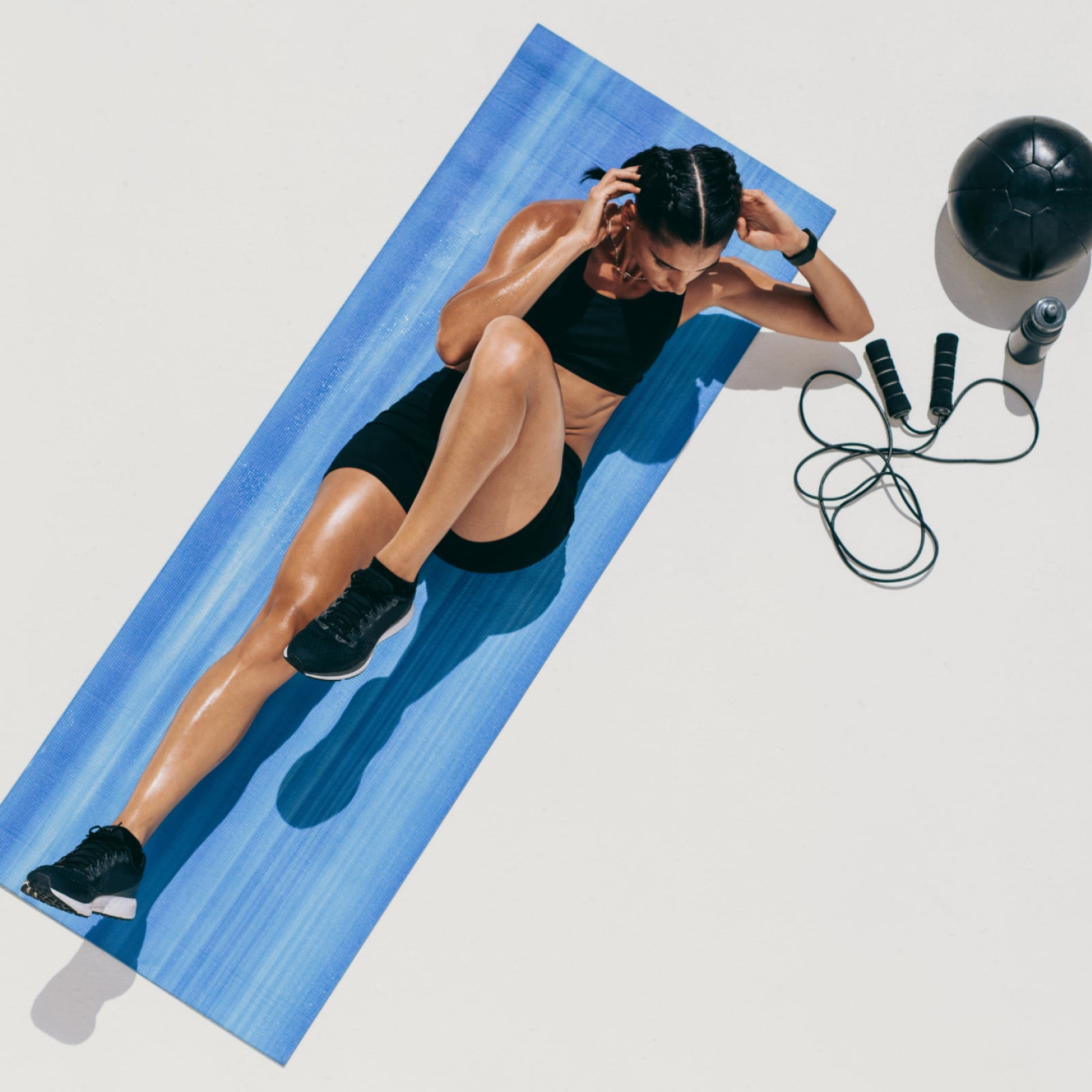 Woman exercising on a blue mat with fitness equipment around her wearing air 5 pro