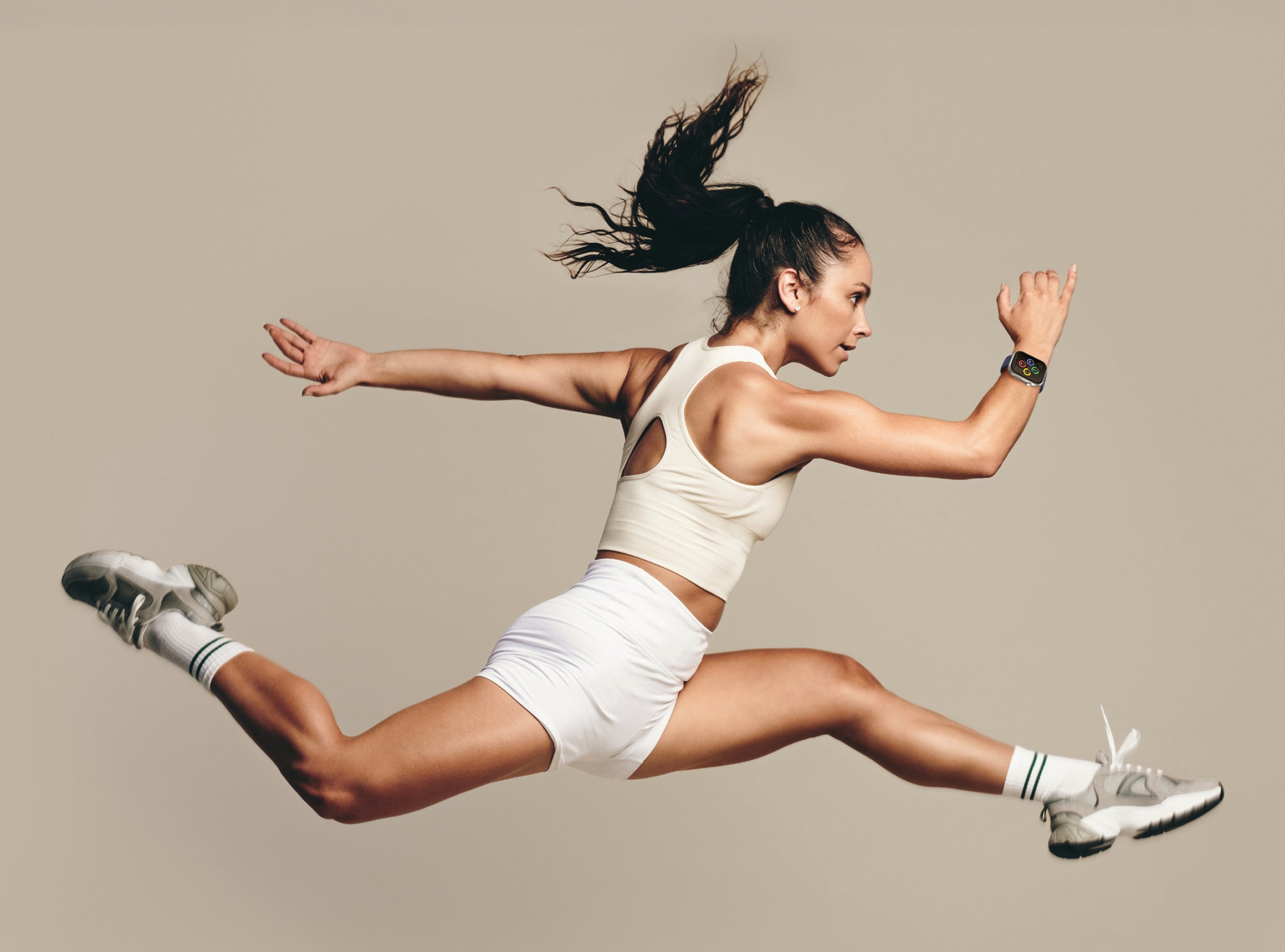 Woman in athletic wear jumping in the air against a plain background