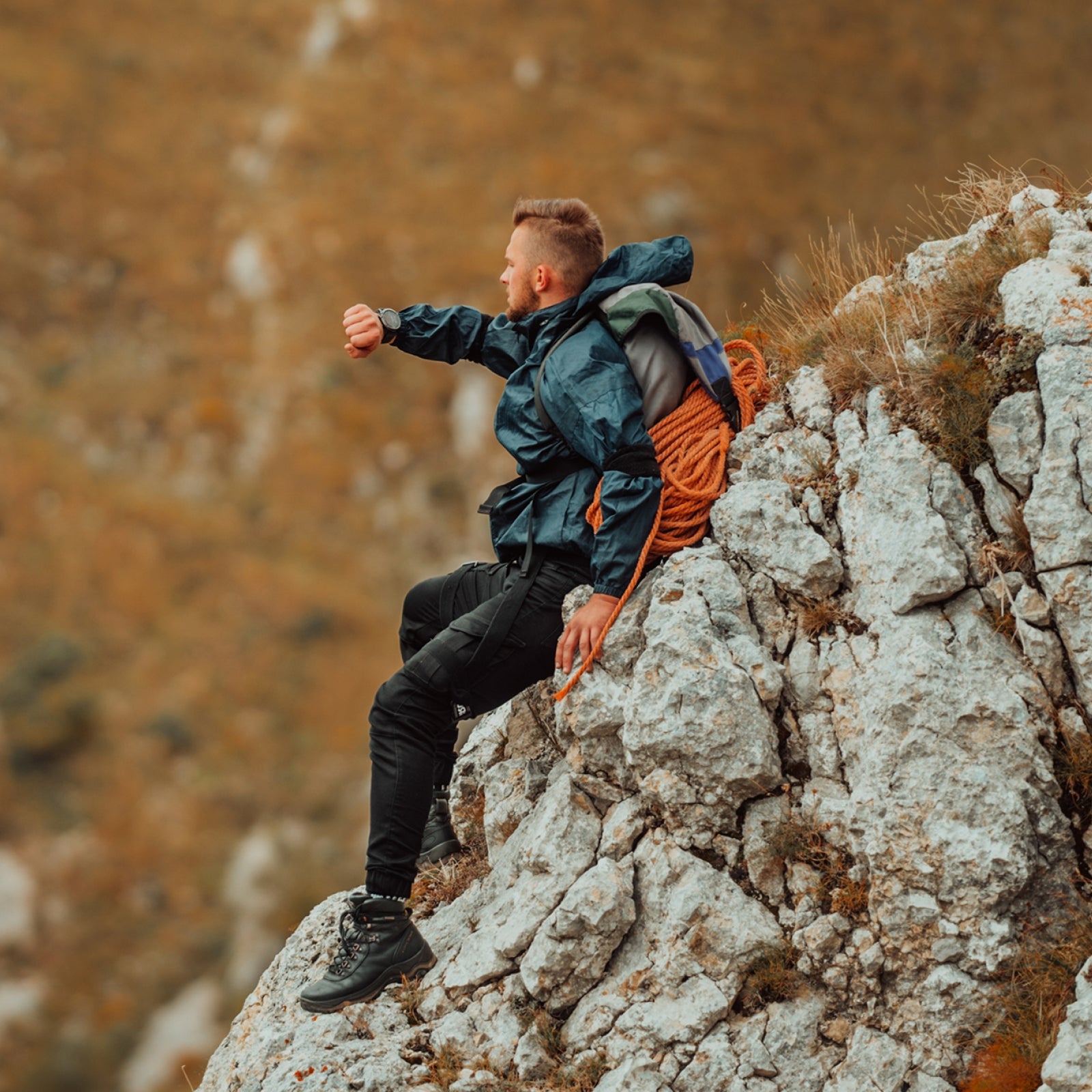 Person sitting on a rocky outcrop with a backpack, surrounded by natural landscape looking at smartwatch